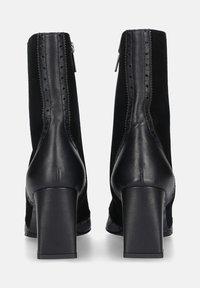 Zwarte enkellaarsjes van een combinatie van suède en leer. Blokhak, ritssluiting en decoratieve geperforeerde randen. Nette textuur.