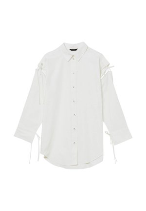 Camicia bianca a maniche lunghe con colletto, chiusura a bottoni e spalle scoperte. Presenta lacci regolabili sulle maniche per un tocco di dettaglio.