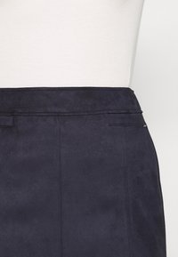 Jupe en suede marine présentant une texture lisse, un léger éclat, une taille plate et un détail de poche à l'arrière.