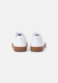 Un par de zapatillas Puma blancas con suelas marrones, mostradas desde la parte trasera sobre un fondo blanco liso.