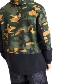 Kamouflagejacka i grön och beige med svarta detaljer och elastisk midja. Har en huva och Timberland-logotyp på baksidan.