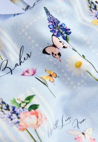 Tessuto blu con stampe floreali e di farfalle, tra cui margherite, lupini e rose rosa, con accenti di testo in corsivo.