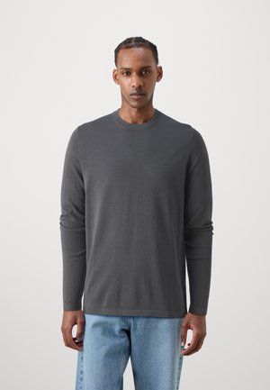 Cămașă din bumbac gri cu mâneci lungi și gât rotund. Țesătura este netedă și ajustată, combinată cu blugi de denim albaștri deschiși.