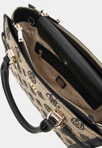 Černá a béžová kabelka s textilním povrchem se vzorem loga, se zipovým uzávěrem a černým interiérem s kapsami a zlatými kovovými akcenty.