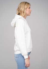 Hvit hettegenser med en avslappet passform, ribbede mansjetter og midjebånd. Har snor i hetten og en lett tekstur.