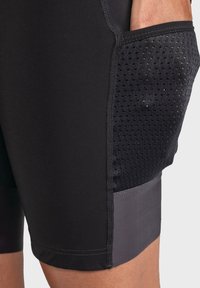 Schwarze sportliche Shorts mit taillierter Passform, ausgestattet mit einer strukturierten Mesh-Tasche und soliden Stoffakzenten. Glattes, dehnbares Material.