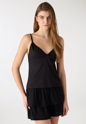 Giovane donna con lunghi capelli castano chiaro che indossa un top nero senza maniche con spalline sottili e una gonna nera a strati.