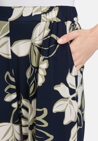 Spodnie w marynarskie wzory z dużymi kwiatowymi motywami w odcieniach kremu i oliwki, z elastycznym pasem oraz bocznymi kieszeniami dla wygody.