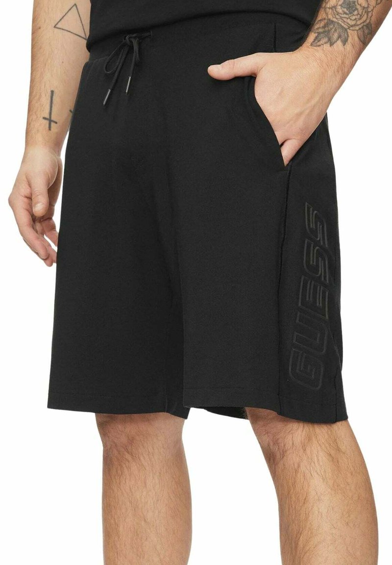 Pantaloncini neri in tessuto morbido, con tasche laterali e logo a rilievo a contrasto sulla gamba sinistra. Vita con coulisse regolabile.