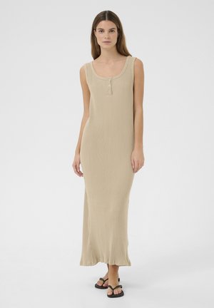 Abito maxi beige a costine con scollo a U, dettagli con tre bottoni e spacchi laterali. Modello che indossa sandali neri piatti.
