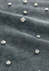 Tessuto grigio a coste con paillettes argentate sparse, caratterizzato da una superficie texture e da un leggero lucore delle paillettes, che mette in risalto gli elementi decorativi.