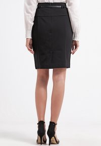 Svart blyertskjol med slät textur, slim fit och detaljerad midja. Kombineras med svarta högklackade skor för en polerad look.