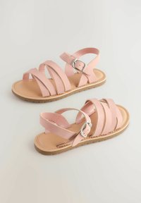 Sandali in pelle rosa con design a strap incrociati, fibbia regolabile alla caviglia e suola in gomma piatta, con una finitura liscia e punta arrotondata.