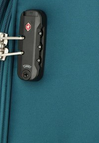 Maleta de tela azul con un candado de combinación TSA negro y un zip de metal, con una superficie texturizada y un detalle del logo visible en el candado.