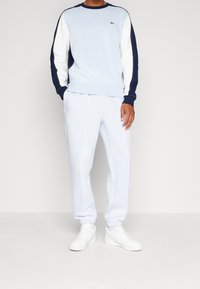 Felpa azzurra chiara con maniche navy e bianche, dotata di un piccolo logo. Abbinata a pantaloni jogger azzurri chiari e scarpe bianche.