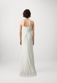 Robe sans manches, longueur au sol, en tissu crème clair. Présente un détail de dos froncé et une fermeture éclair à l'arrière. Texture lisse.
