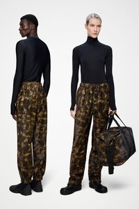 Μαύρο τοπ με μακριά μανίκια σε συνδυασμό με καφέ παντελόνια jogger με καμουφλάζ σχέδιο και μαύρα παπούτσια. Το μοντέλο κρατά μια τσάντα duffel που ταιριάζει, με ανθεκτικούς ιμάντες.