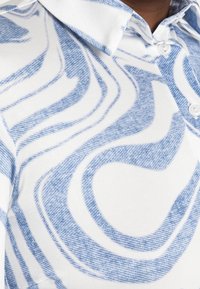 White shirt with large, abstract blue swirl patterns and a collar, showing button details near the neck and chest area.