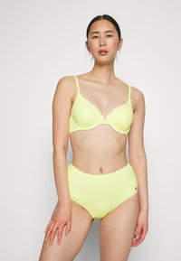Conjunto de lingerie amarelo com um design de borda recortada tanto no sutiã quanto nas calcinhas de cintura alta, feito de um tecido suave.