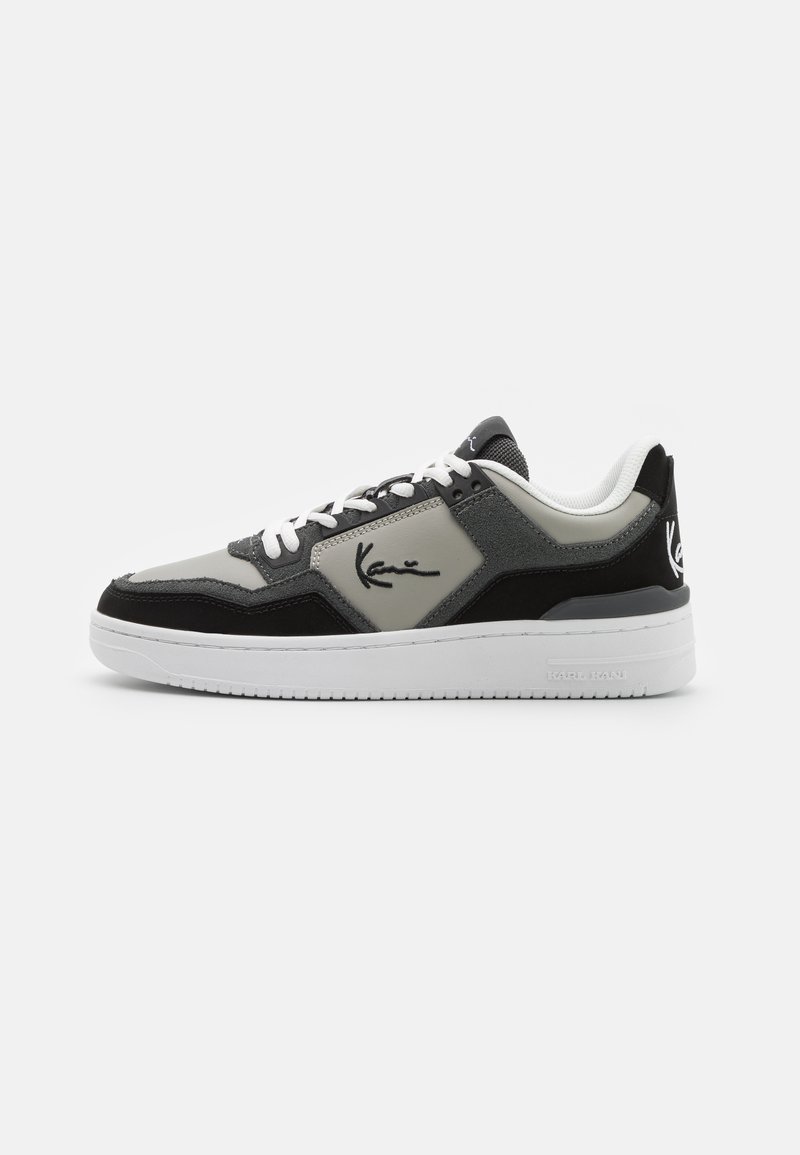 Baskets de sport présentant un mélange de matériaux noir, gris et blanc, avec des textures en suède et synthétiques. Comprend un logo détaillé sur le côté.