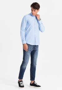 Camisa de botones a rayas azul claro y blanca, de mangas largas, combinada con jeans de mezclilla oscura y zapatillas negras con suelas blancas.