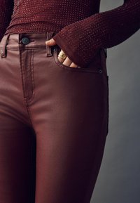 Bordeaux smala jeans med en slät textur, med framfickor, knäppning och kontrasterande sömmar. Åtföljs av en figurnära topp med dekorationer.