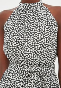 Černo-bíl dress s halter krkem a přiléhavým pasem, který zdobí texturovaný vzor malých čtverců a mašle v oblasti pasu.