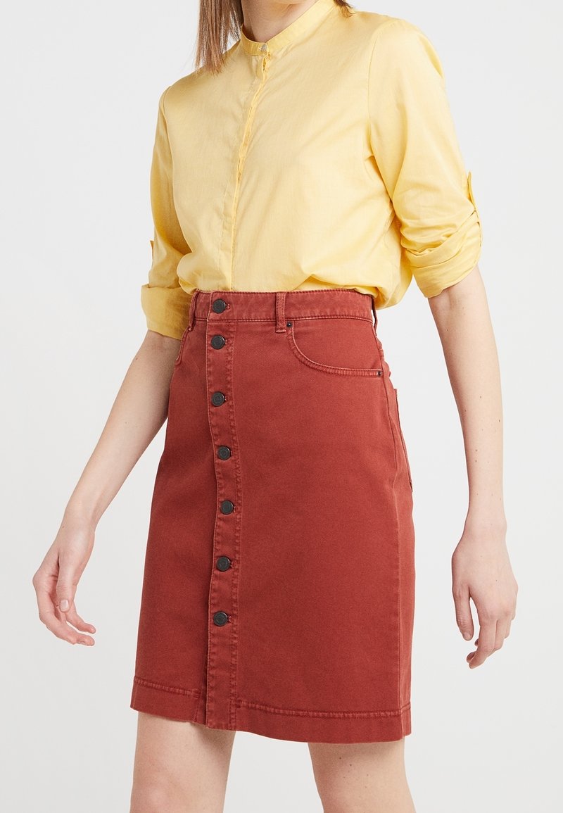 Röd denimkjol med rak skärning, med en knappstängning fram och två sidofickor. Bärs tillsammans med en gul skjorta med krage.