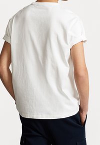 Vit bomullstshirt med kort ärm och rund halsringning, med uppvikta ärmar och en avslappnad passform utan synliga logotyper eller mönster.