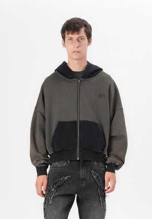 Sweat à capuche zippé surdimensionné en vert foncé et noir, avec une poche contrastante, des poignets en côtes et une texture douce.