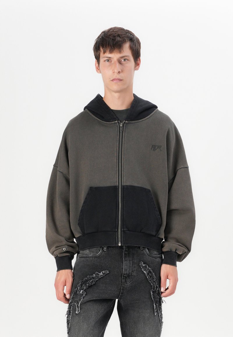 Fato de capuz oversized com fecho éclair em verde escuro e preto, apresentando um bolso em contraste, punhos canelados e uma textura suave.
