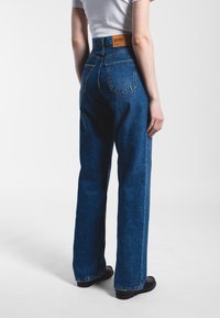 High-waisted blue denim jeans with a slight fade, two back pockets, and a brown leather label on the waistband. Flat front and wide legs.
