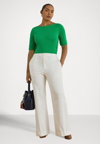 Πράσινο τοπ με κοντά μανίκια και λαιμόκοψη bateau, συνδυασμένο με εκρού παντελόνι φαρδιάς γραμμής. Το μοντέλο κρατά μια σκουρομπλε τσάντα με καφέ λεπτομέρεια.