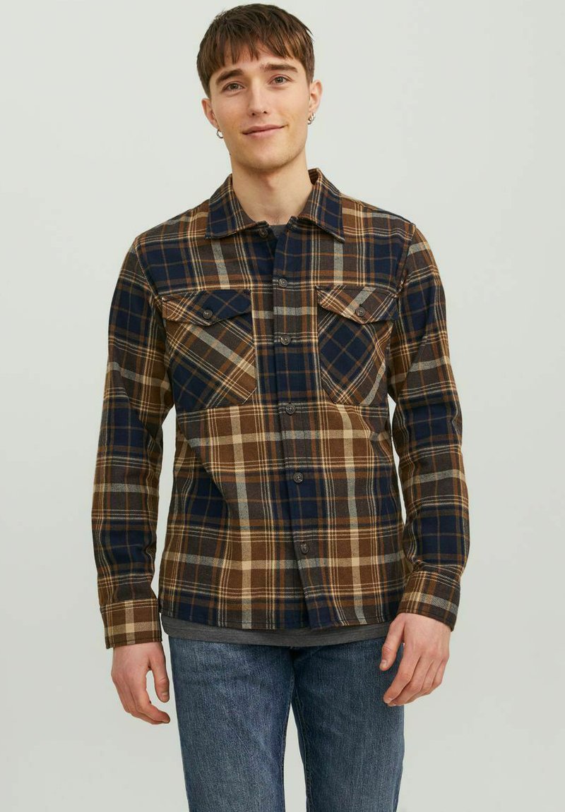 Camisa de cuadros en tonos marrón, azul marino y gris; presenta dos bolsillos en el pecho, cierre frontal con botones y un cuello con solapa. Textura de tela suave.