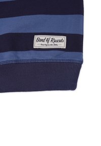 Tummansininen ja vaaleansininen raitapaitainen svetari, joka on valmistettu pehmeästä puuvillasta. Tässä paidassa on ribbaatut hihansuut ja selkeästi näkyvällä "Band of Rascals" -tarralla varustettu merkki.