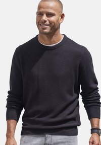 Dunkler Pullover aus strukturiertem Strickstoff, mit Rundhalsausschnitt, gerippten Bündchen und Saum, kombiniert mit hellgrauen Jeans.