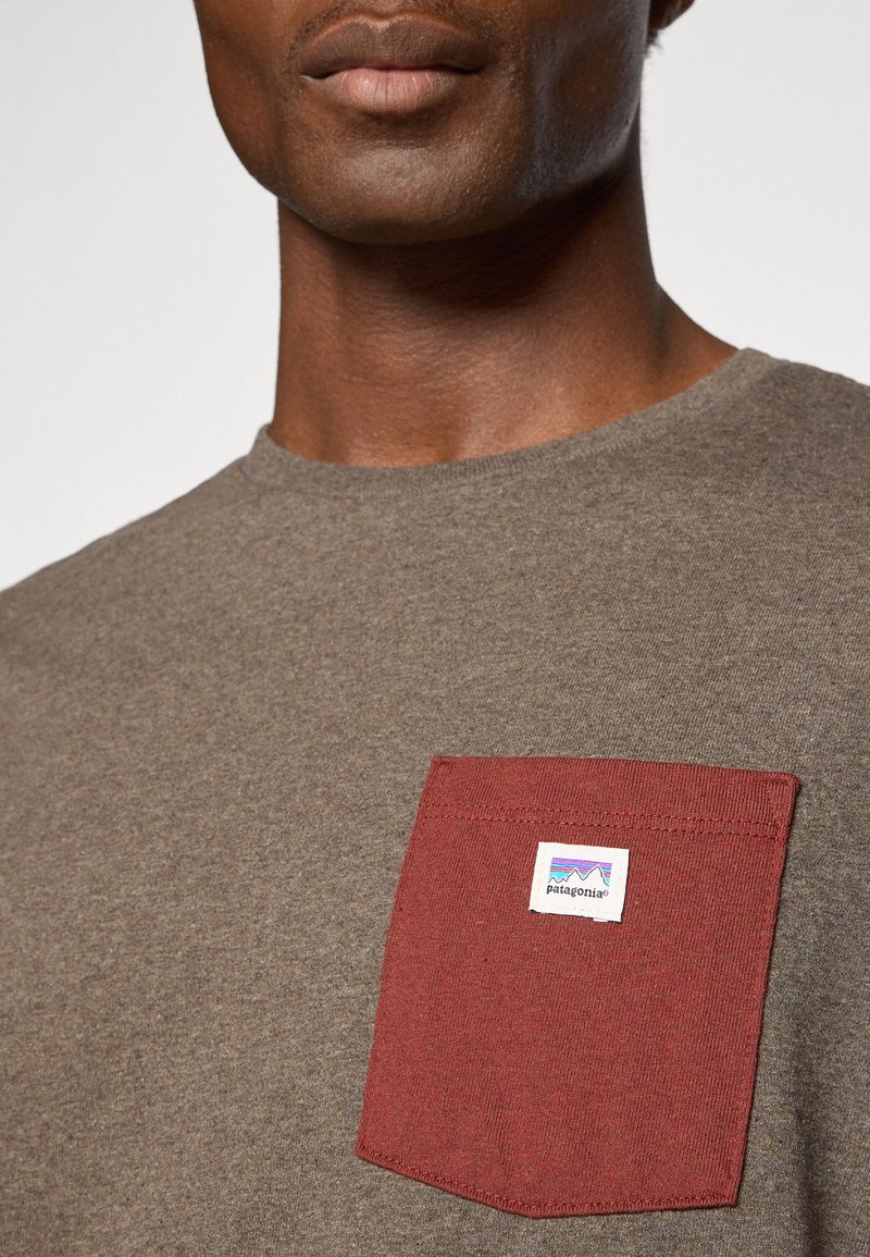 Bruine katoenen t-shirt met een ronde halslijn en een kastanjebruine borstzak met een Patagonia-logo. Glad textuur, casual ontwerp.