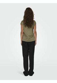 Top verde oliva de manga corta con un corte relajado, combinado con pantalones negros holgados. El conjunto presenta un diseño simple y sin adornos.