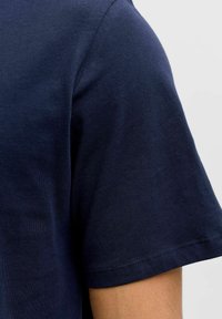Camiseta de color azul marino con mangas cortas, hecha de algodón suave. Presenta un cuello redondo y una textura suave, mostrando detalles de costura.