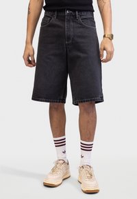 Sorte denimshorts med lige snit, fem lommer og kontrastsyet. Kombinationen er med cremefarvede sneakers og stribede hvide sokker.