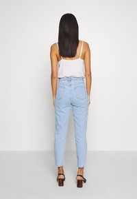 Jeans de tiro alto en azul claro con pierna ajustada, con bolsillos traseros y detalles de costura sutiles, combinados con una blusa sin mangas blanca y tacones negros.