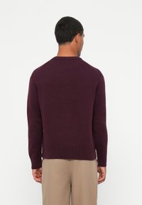 Πουλόβερ σε σκούρο μωβ πλέξη με στρογγυλή λαιμόκοψη και ριμπ μανσέτες. Μαλακή υφή, εφαρμοστή γραμμή, και στρίφωμα που καταλήγει στη μέση.