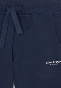 Marineblauwe sweatpants gemaakt van zacht materiaal, met een tailleband met trekkoord en een klein wit logo dat op de zijkant is gedrukt.