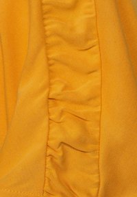 Närbild av ett klart gult tyg med en centrala del som har rynkad eller veckad textur och släta sidopaneler.