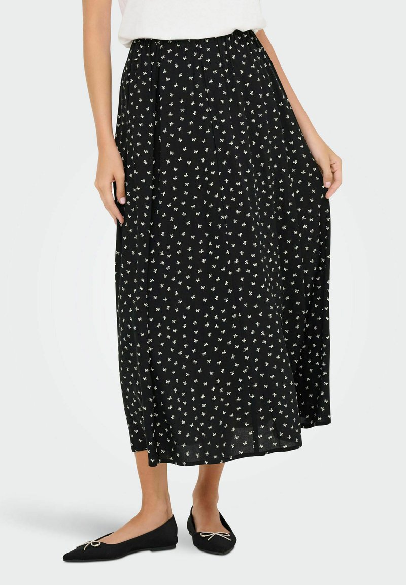 Jupe maxi noire à motifs floraux en tissu léger, dotée d'une taille élastique. Associée à des ballerines noires à bout pointu.