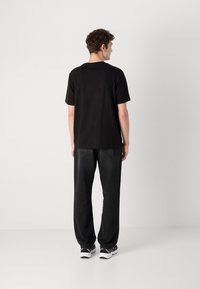 Black short-sleeve t-shirt, relaxed fit, smooth texture, paired with dark gray loose-fit pants, worn with black and white sneakers.