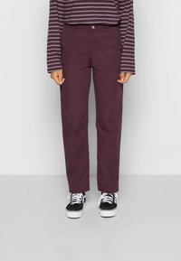 Maroon cotton pants with a straight cut, featuring front pockets and a button detail. Paired with black and white patterned sneakers.