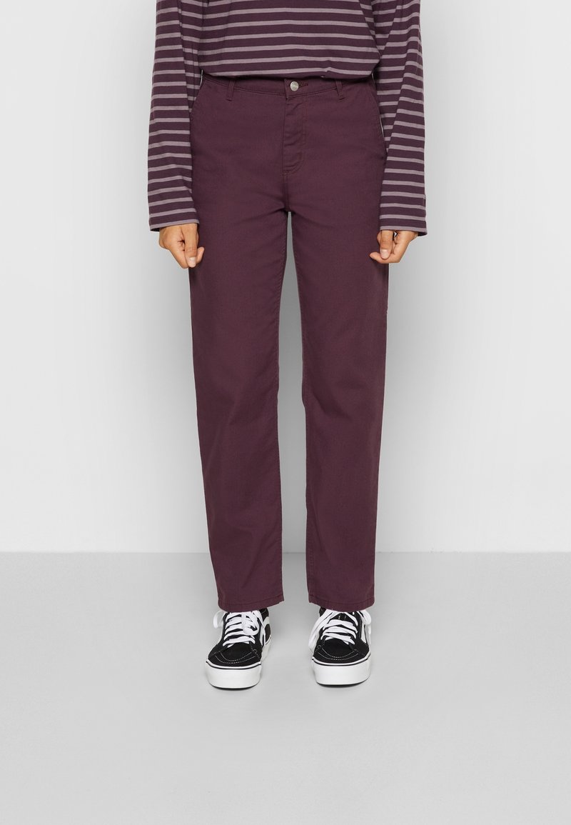 Maroon cotton pants with a straight cut, featuring front pockets and a button detail. Paired with black and white patterned sneakers.