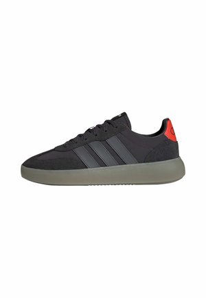 Sort lavtop sneaker med grå sål, tre mørke striber på siden, sorte snørebånd og en rød hæltkappe.
