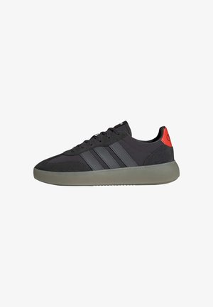 Schwarzer Low-Top-Sneaker mit grauer Sohle, drei dunklen Streifen an der Seite, schwarzen Schnürsenkeln und rotem Fersenlasche.